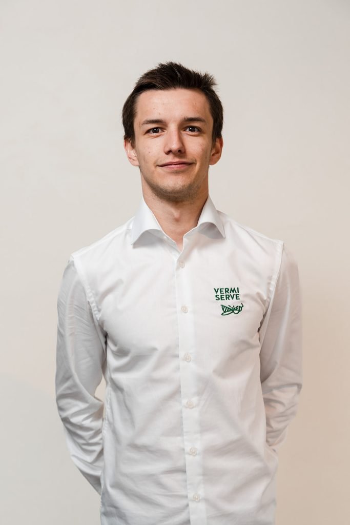 Man met donker haar in wit overhemd met Vermi Serve logo, staande voor neutrale achtergrond.